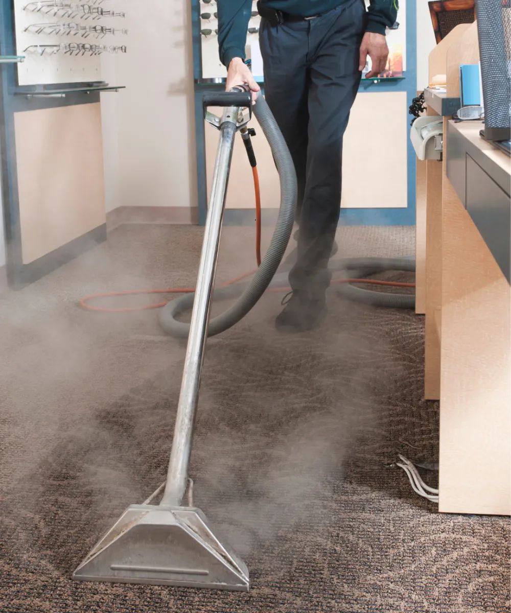 A man using a vacuum cleaner to clean a carpet at a glasses store.